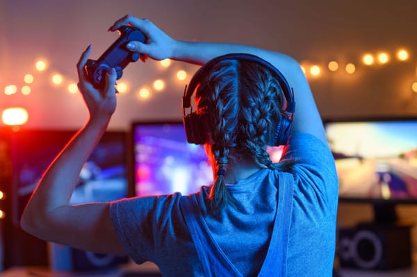 Gamer or streamer girl at home in a dark room with a gamepad playing video games with friends online. Young man sits in front